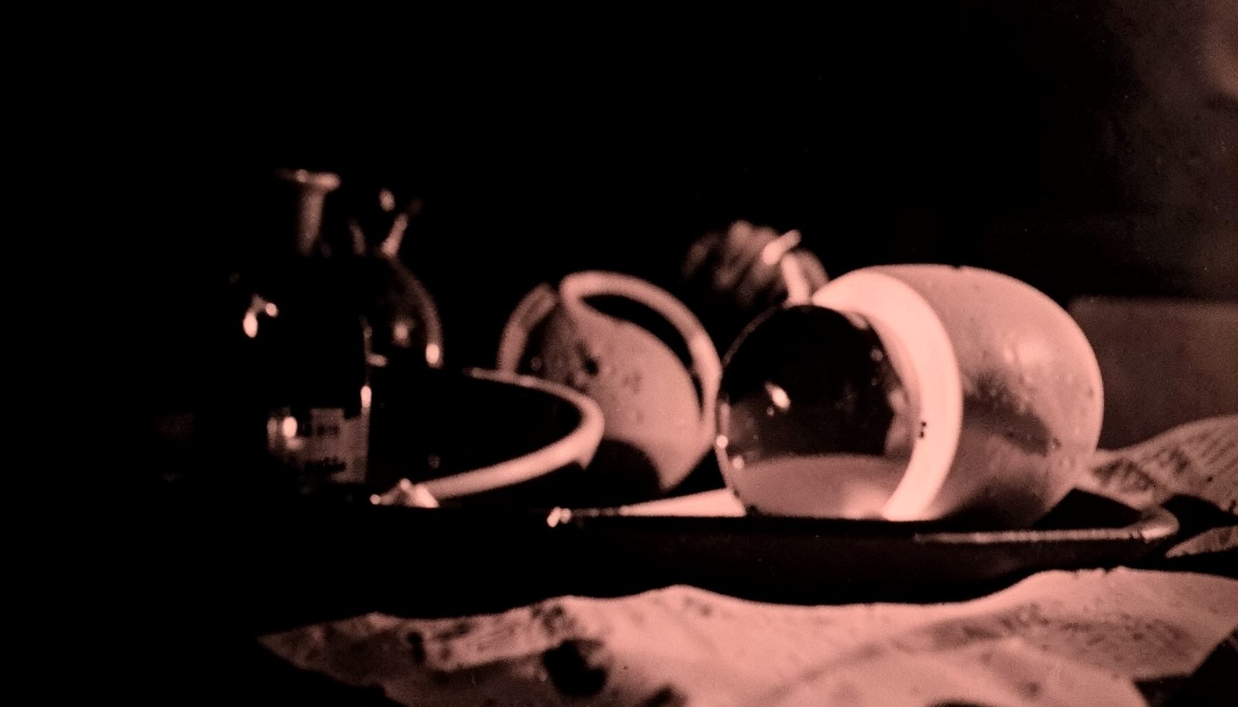 A duotone photograph in deep black and pale coral showing a quiet still-life arrangement with soft shadows