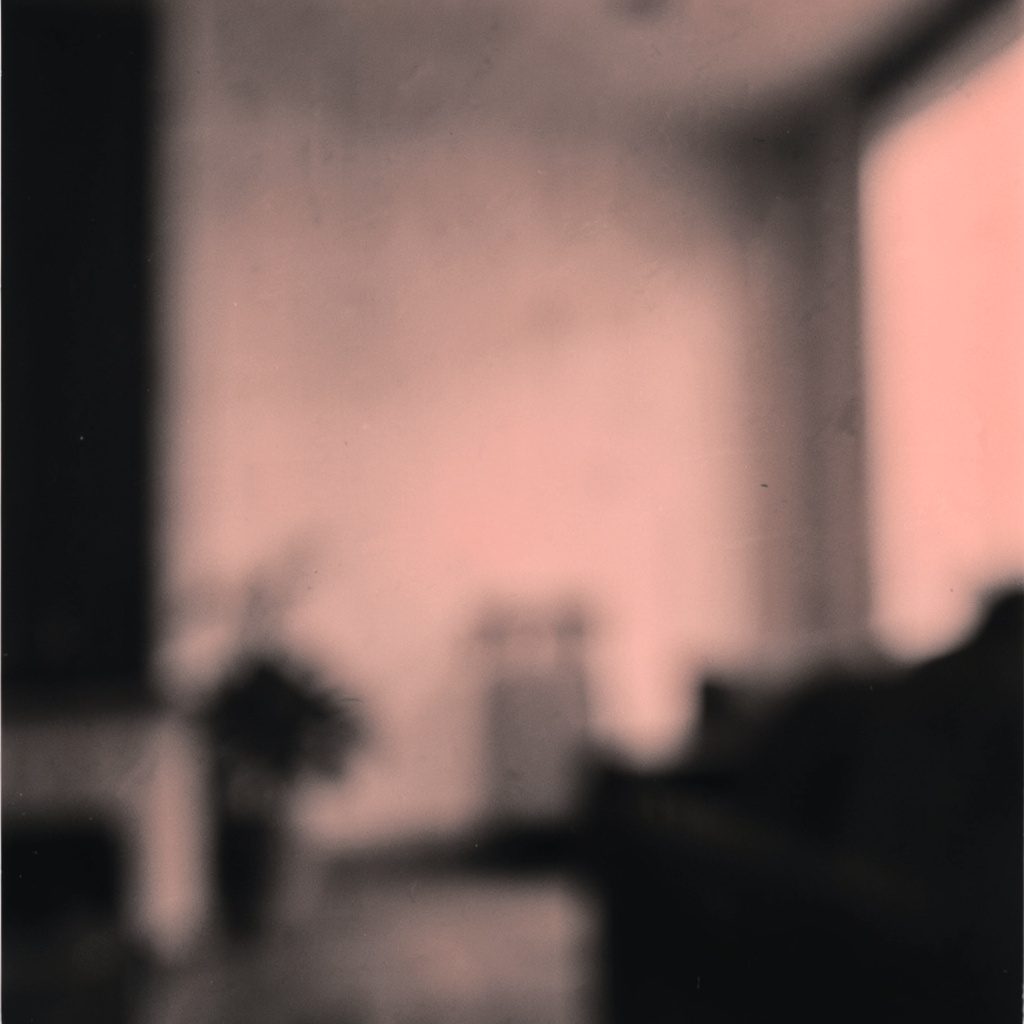 A simple duotone photograph in dark charcoal and soft coral tones showing an abstract blurred interior space with a calm, quiet mood